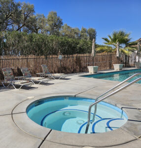 View of hot tub and lounge chairs, pool in background